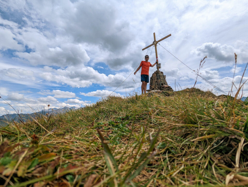 Ein Wanderer steht am Gipfelkreuz des Zwölferkogels unter blauem Himmel, ein Erfolgserlebnis beim Wanderurlaub im Nationalpark Hohe Tauern.
