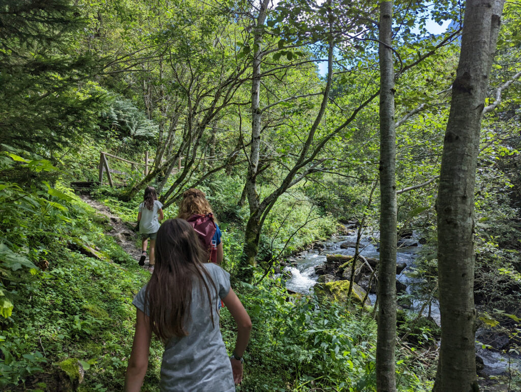Familie wandert auf einem schmalen Pfad entlang eines Bachs in der grünen Schösswendklamm, ideal für einen Familienurlaub in den Hohen Tauern.