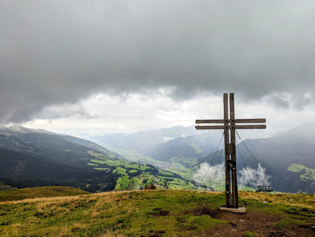 Gipfelkreuz auf dem Resterkogel mit nebelverhangenen Bergen und Tälern im Hintergrund, beeindruckende Aussicht im Nationalpark Hohe Tauern.