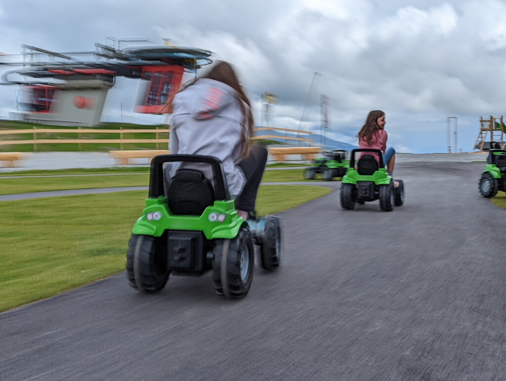 Kinder fahren auf grünen Kettcars auf einer Rennstrecke am Resterkogel, Spaß für den Familienurlaub im Nationalpark Hohe Tauern.