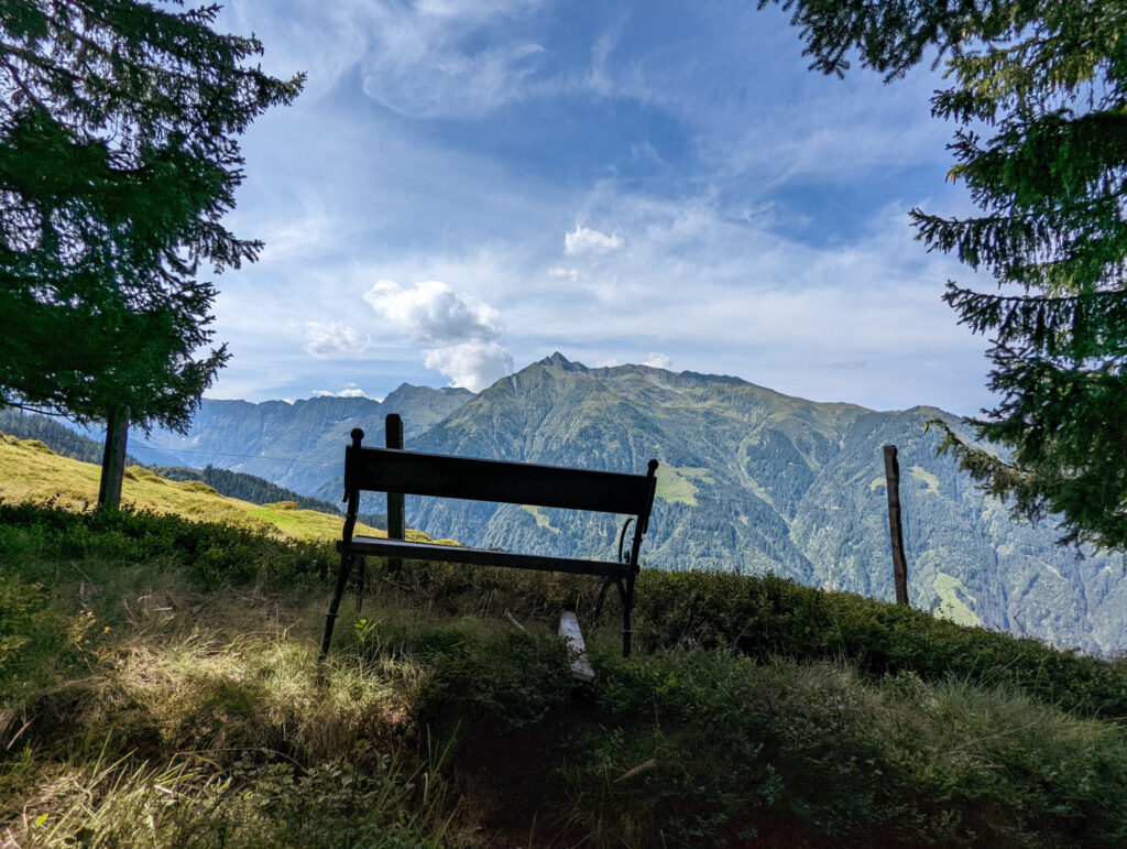 Eine Holzbank mit Panoramablick auf die Berge am Wanderweg zum Zwölferkogel, ideal für eine Pause im Nationalpark Hohe Tauern.