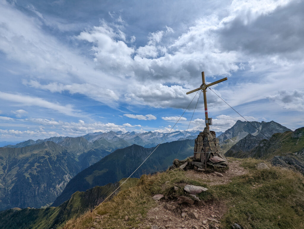 Gipfelkreuz auf dem Zwölferkogel mit Blick auf die schneebedeckte Venedigergruppe, ein Highlight beim Wanderurlaub im Nationalpark Hohe Tauern.