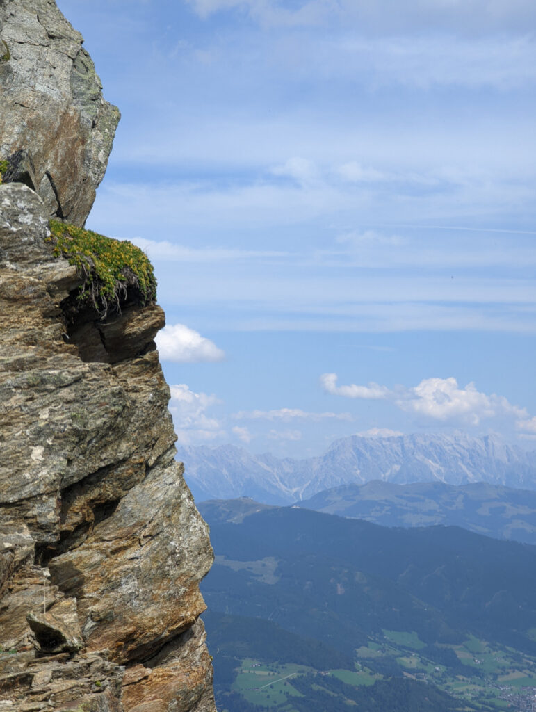 Spektakulärer Tiefblick von einer Felswand auf ein weites Tal mit Bergen am Horizont, Aussicht während der Wanderung im Nationalpark Hohe Tauern.