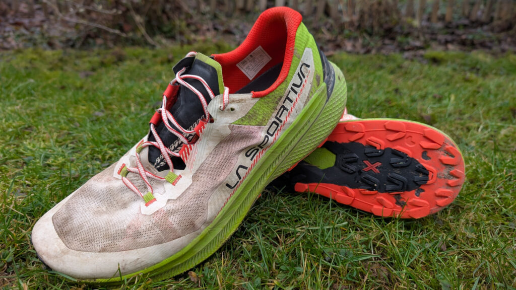 Nahaufnahme des La Sportiva Prodigio Trailrunning-Schuhs in Weiß-Grün auf einer Rasenfläche, Fokus auf das Mesh-Obermaterial und die Schnürung.