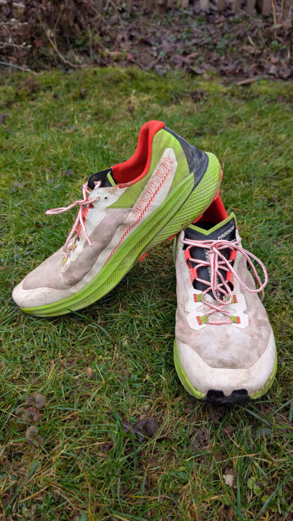 Seiten- und Frontansicht des La Sportiva Prodigio Trailrunning-Schuhs auf Gras, der die XFlow-Dämpfung und das Design zeigt.