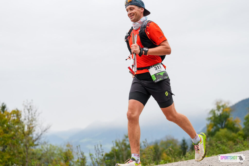Trailrunner mit Faltstöcken und La Sportiva Prodigio Schuhen beim Abstieg auf einem Schotterweg in den Alpen.