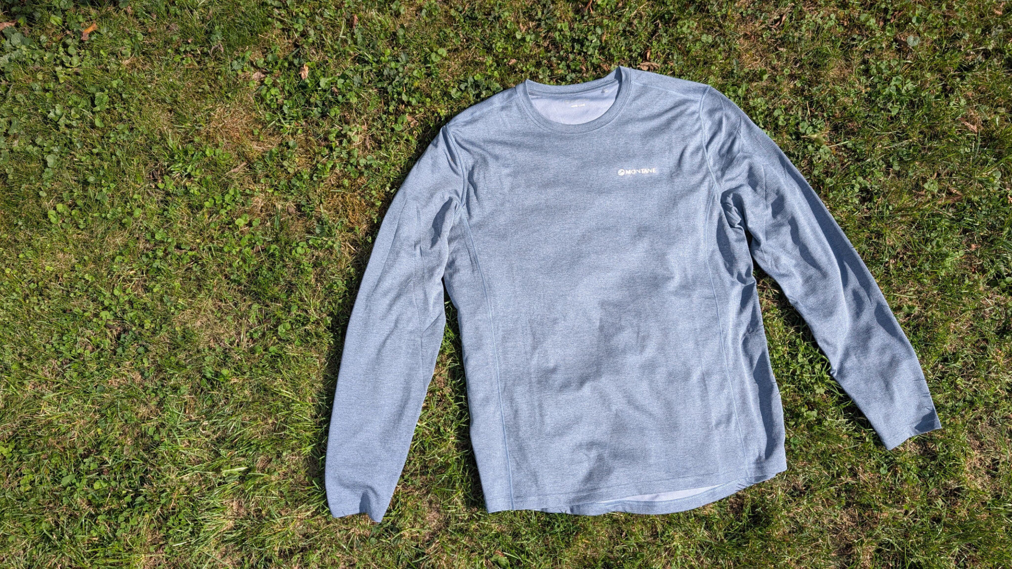 Vorderansicht des Montane Dart Long Sleeve T-Shirt in meliertem Blau, flach auf grünem Gras ausgebreitet für den Praxistest.